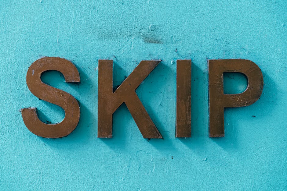 A close-up photograph of the word 'SKIP' displayed in large, three-dimensional brown metal letters mounted on a textured, light blue painted wall. The letters have a matte finish with slight variation